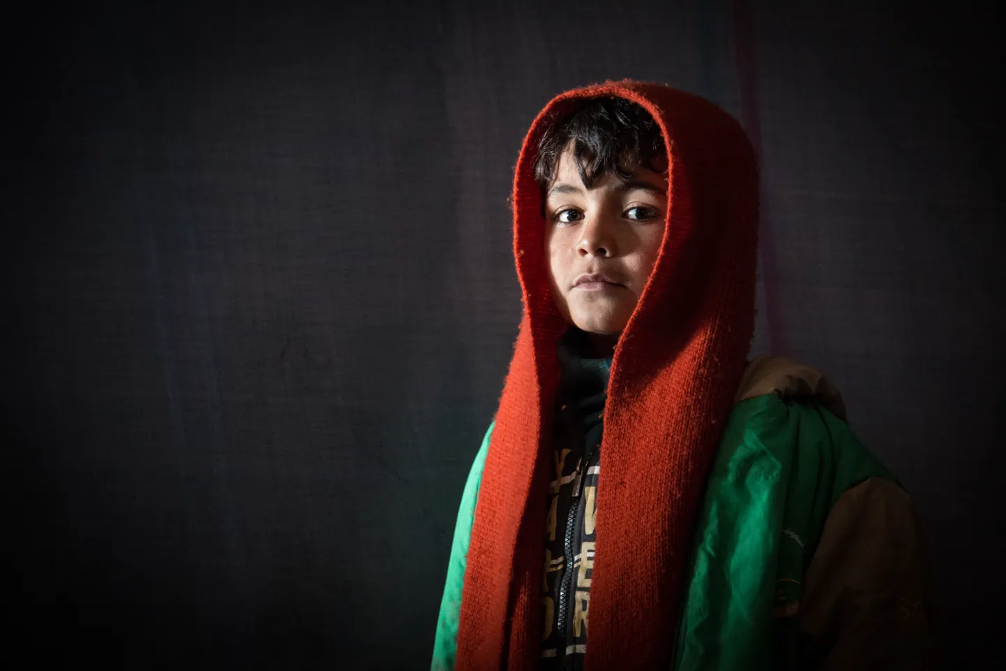A young boy wearing a scarf on his head, in the dark