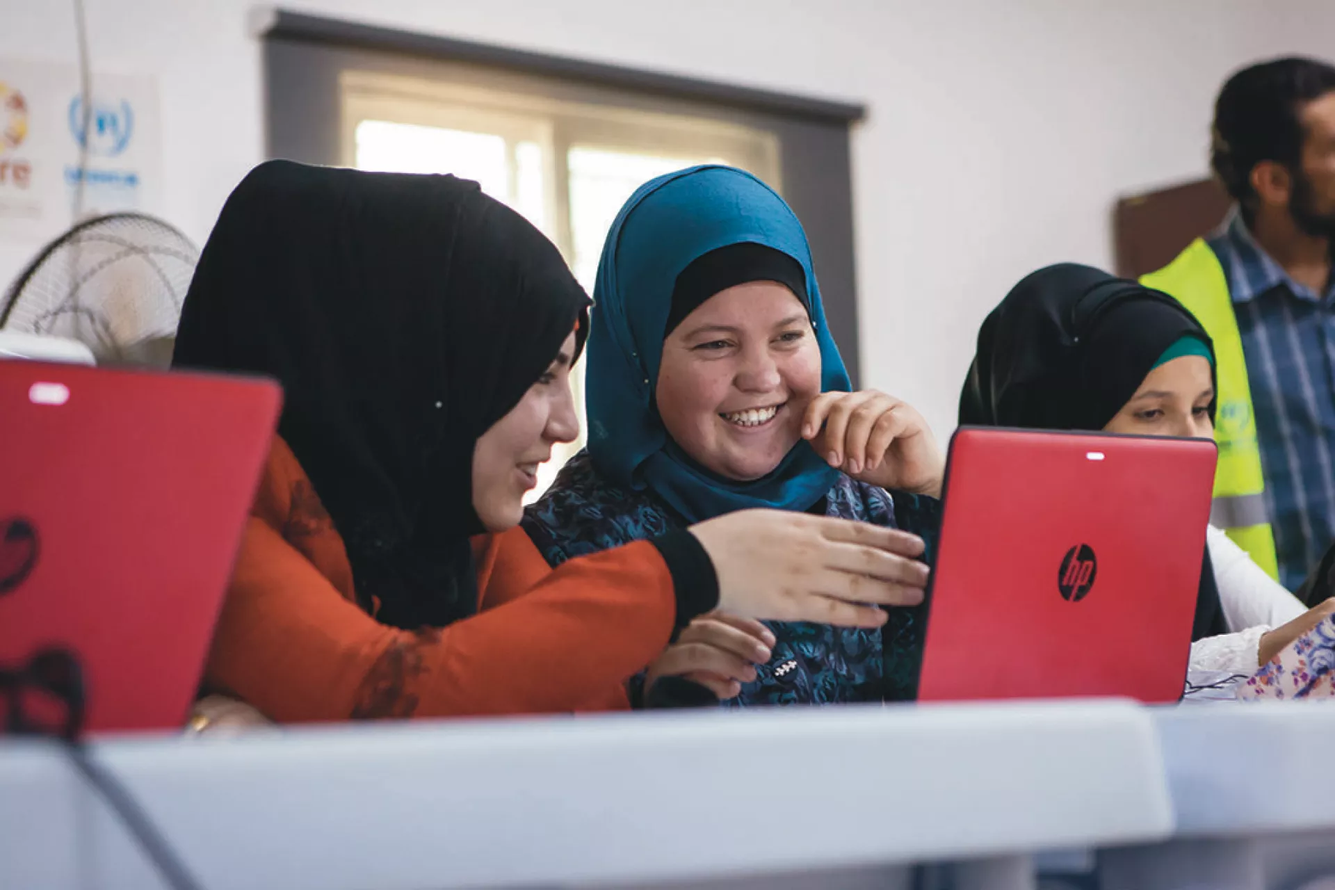 Three adolescent girls working on a computer and laughing, with their instructor in the back