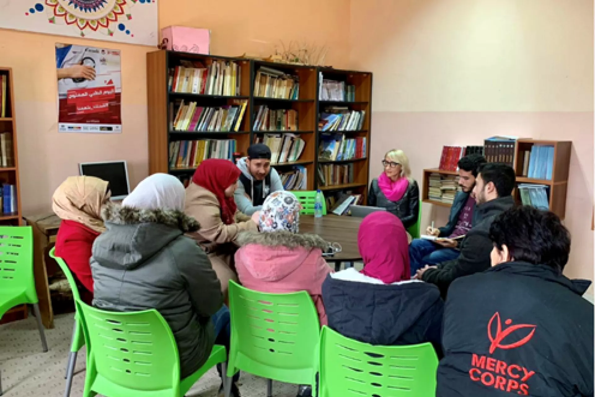 Mercy Corps, UNICEF and Leila Toplic are planning the No Lost Generation Tech Summit in Ajloun, sitting around a table, with book shelves behind.