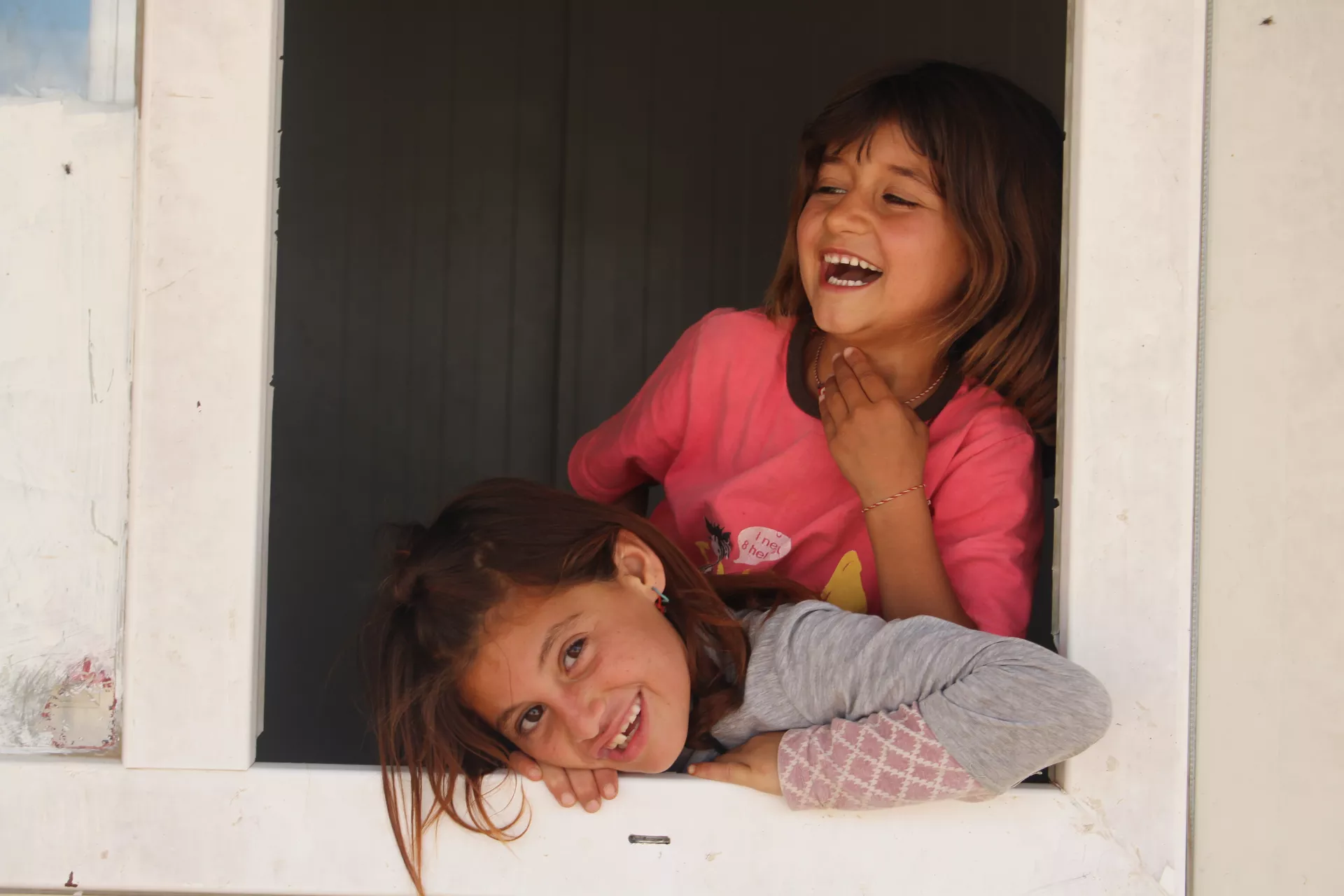 Two girls smiling at the edge of a window