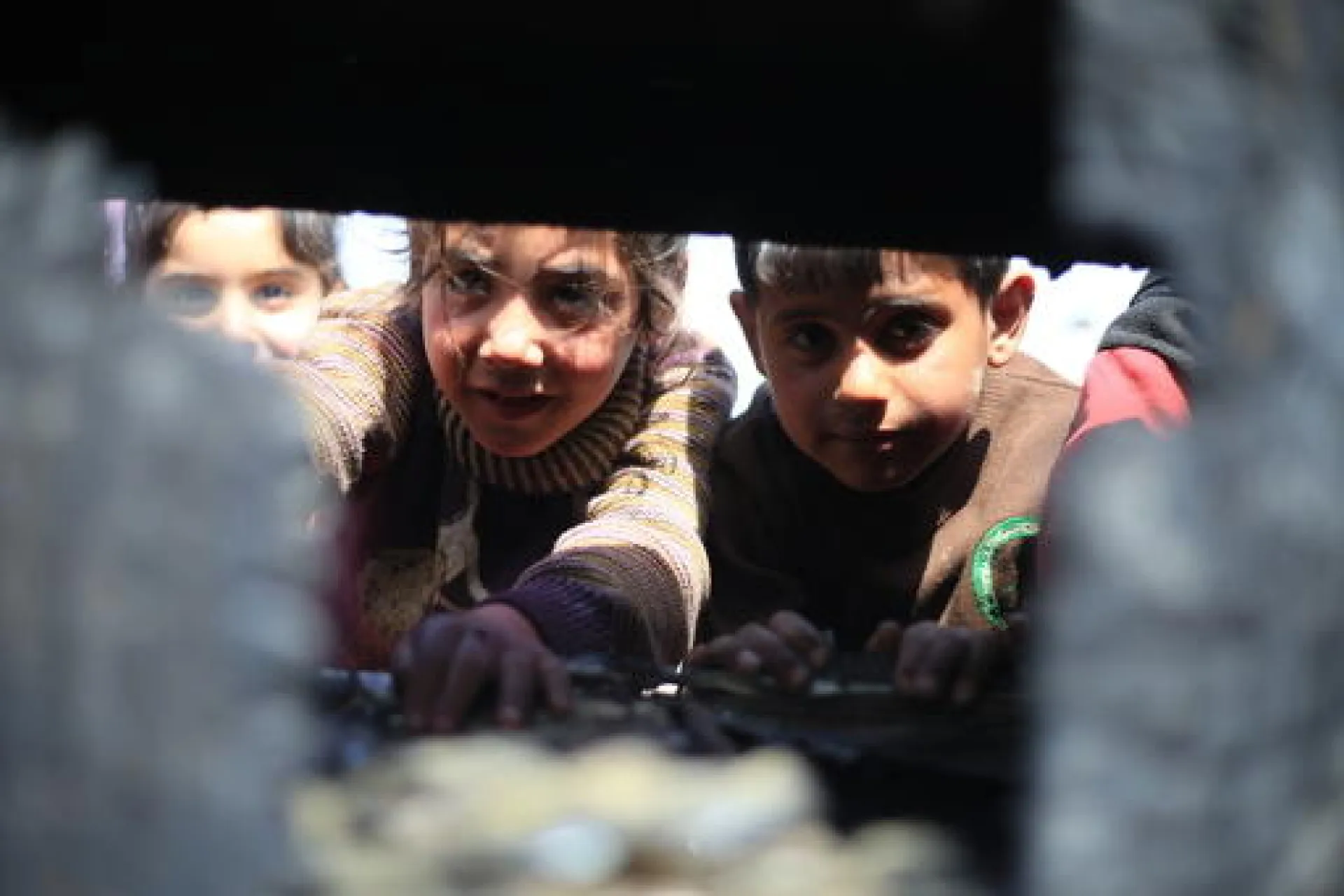 Two girls and one boy seen through an opening in a wall