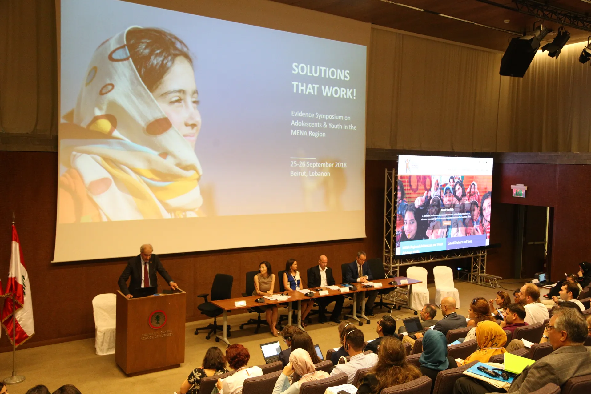 Four presenters in front of a crowd with a powerpoint presenting the summit behind them