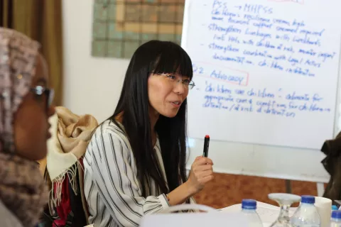 A woman sitting at a table speaking, behind a flip chart
