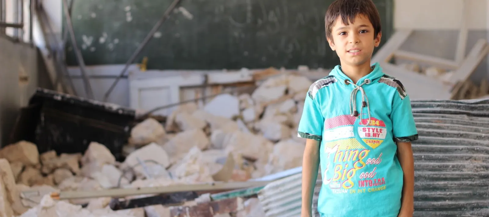 A young boy is standing in a class that was destroyed