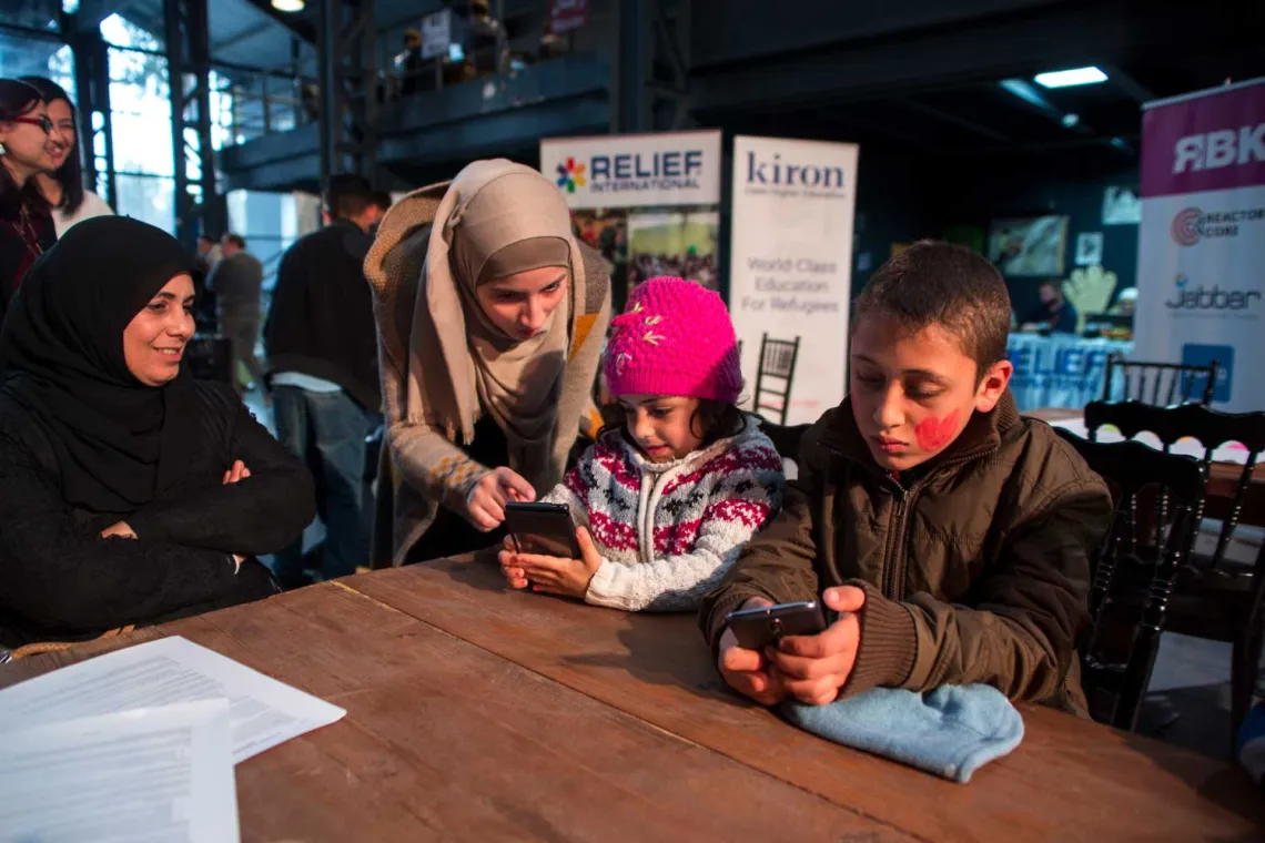 Two women assisting two children using mobile phones