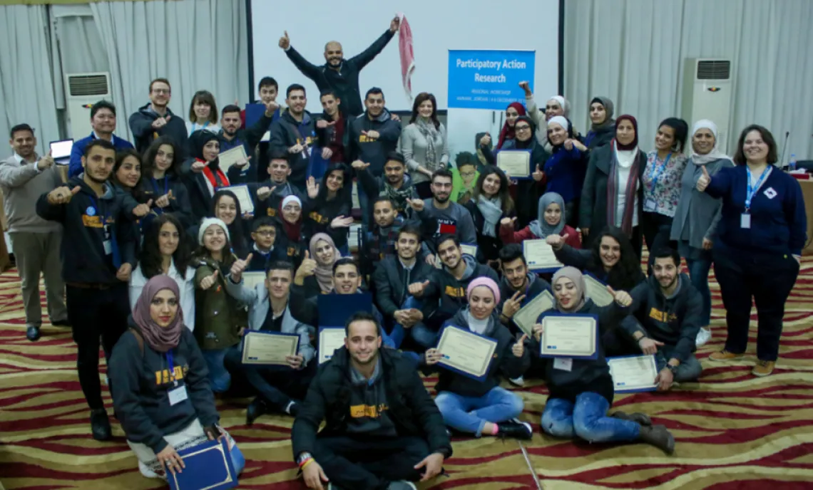A group picture of many young people sitting behind a "Participatory Action Research Banner"