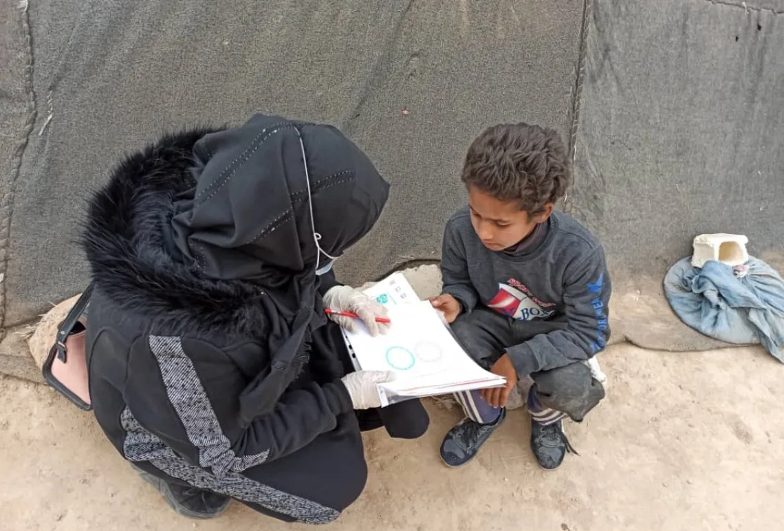 A woman is teaching a children outside, sitting on the ground