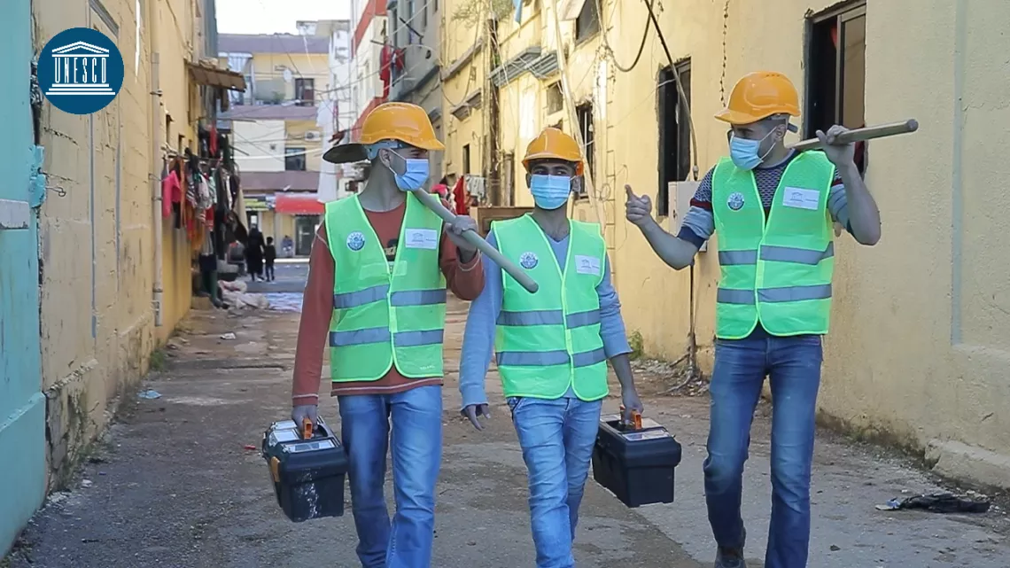 Three young men walking in Beirut after the Blast, wearing construction helmet and holding shovels