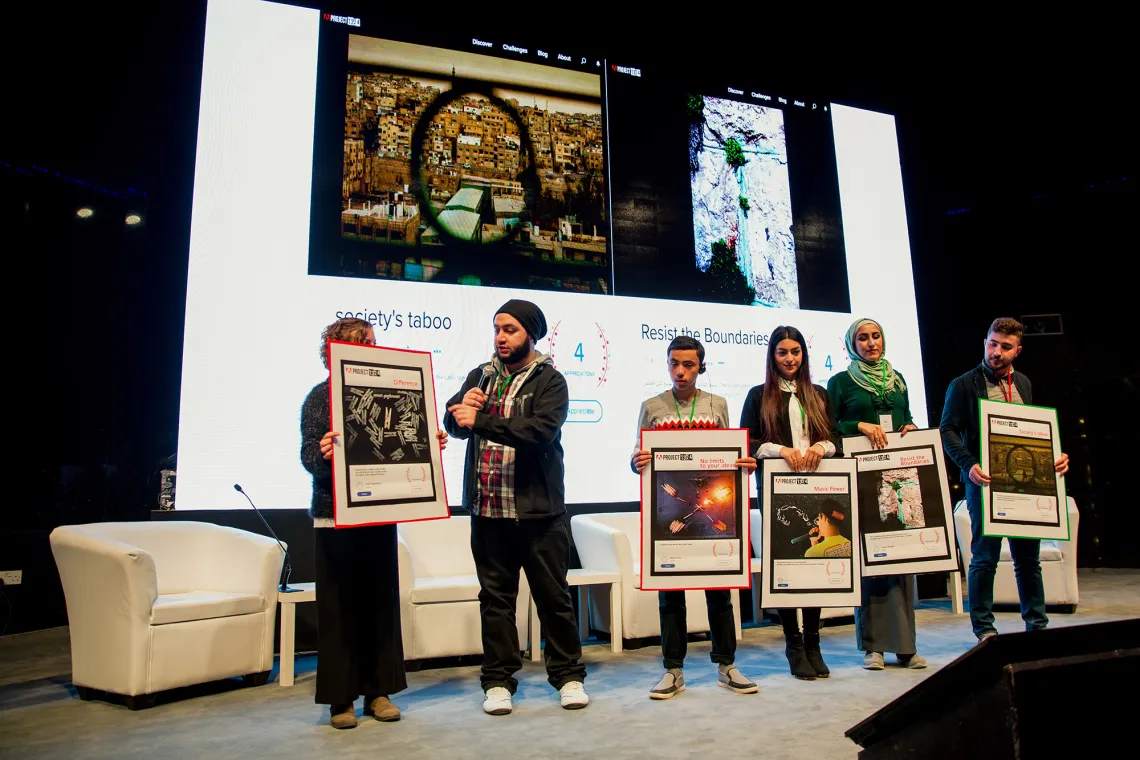 A man is presenting four women who are holding frames on a stage