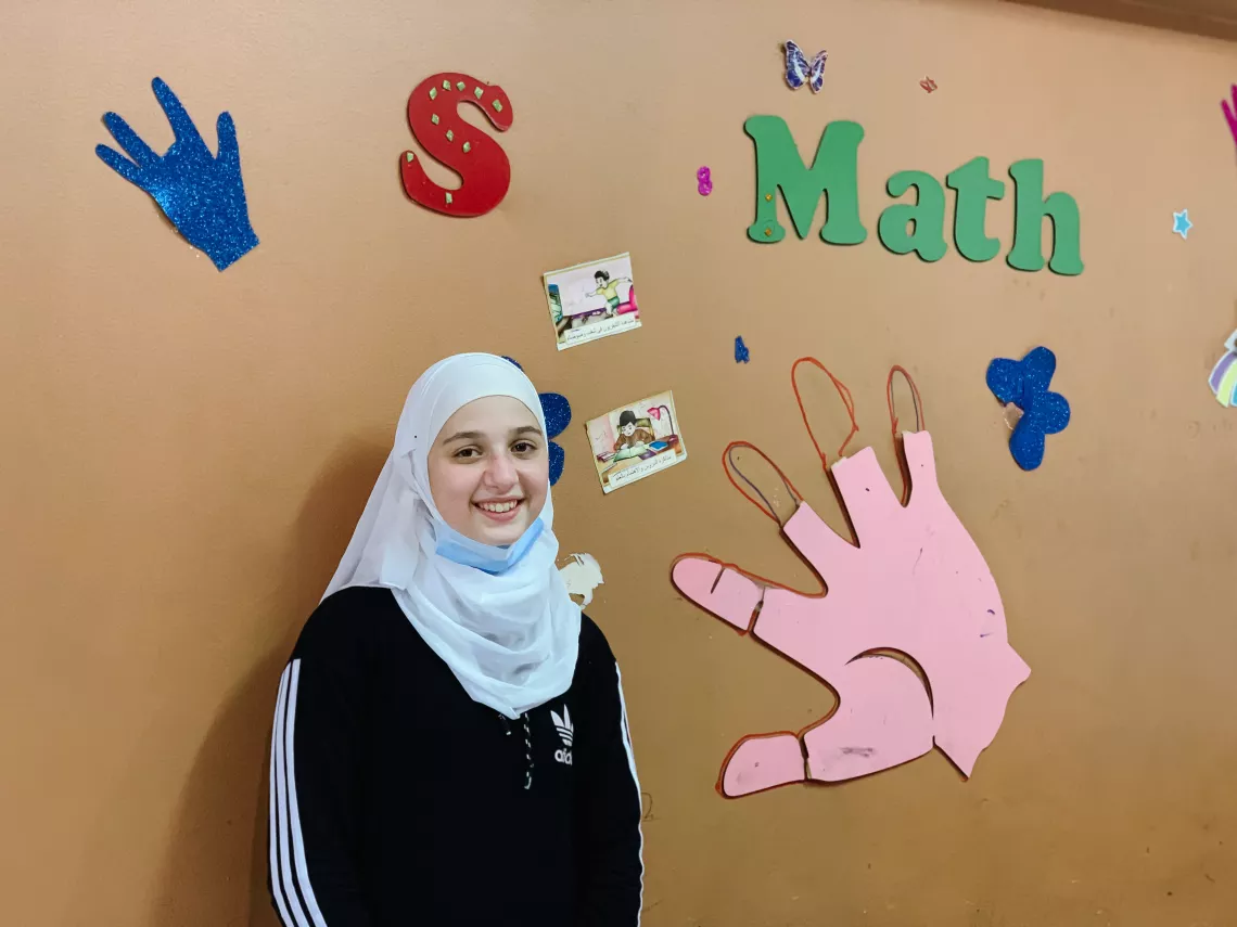Picture of a young girl in front of a school wall where it is written "Maths"