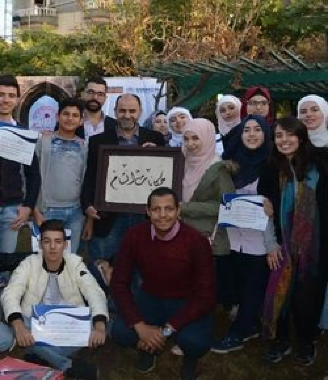A group of young Syrian women and men outside with one man holding a placard.