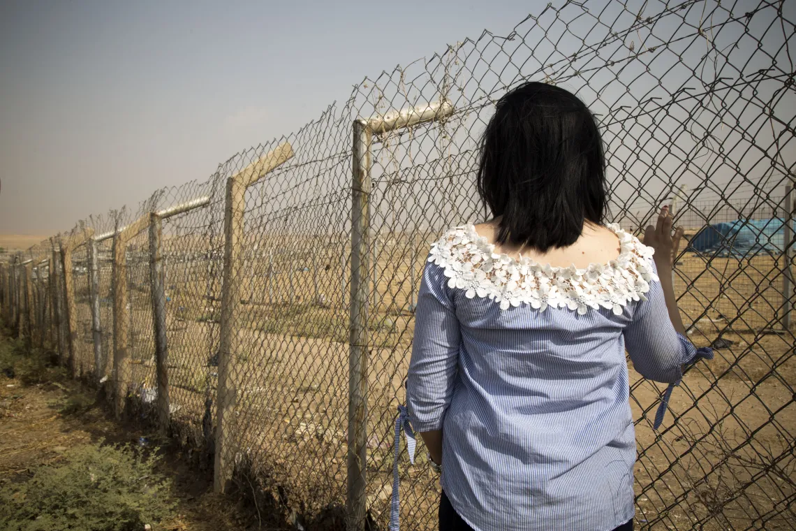 A young girl seen from the back facing a fence