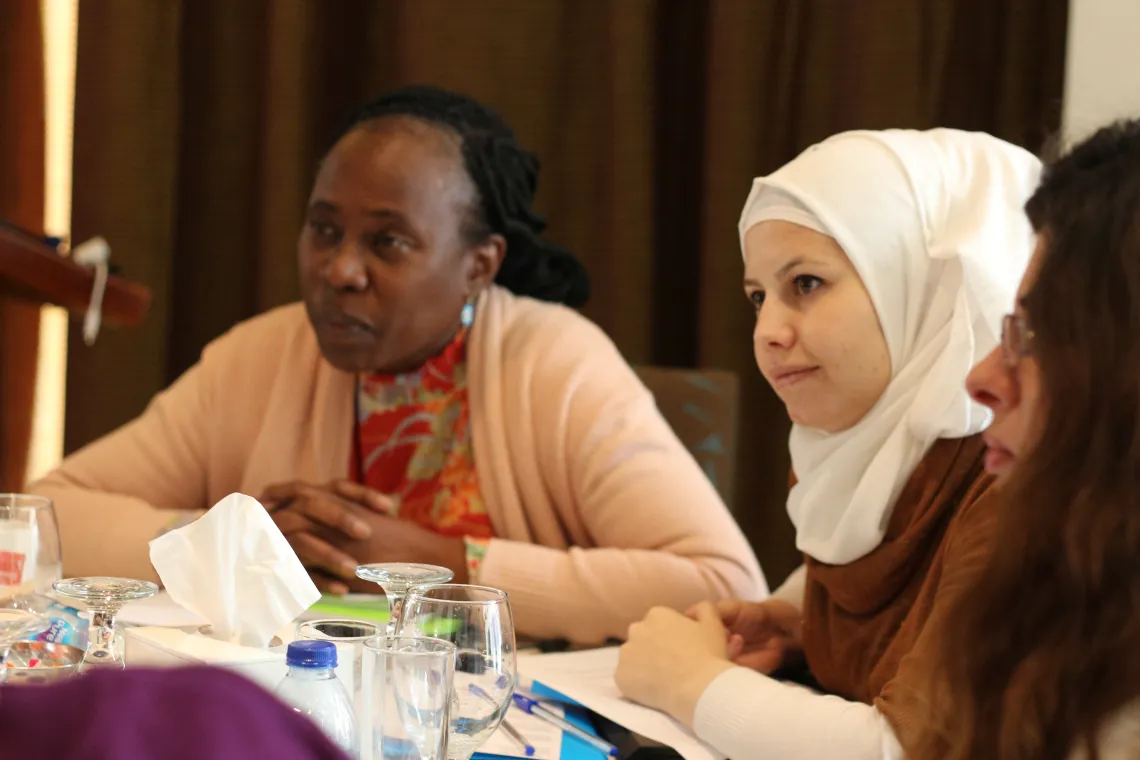 Two woman are sitting at a table and listening to other participants
