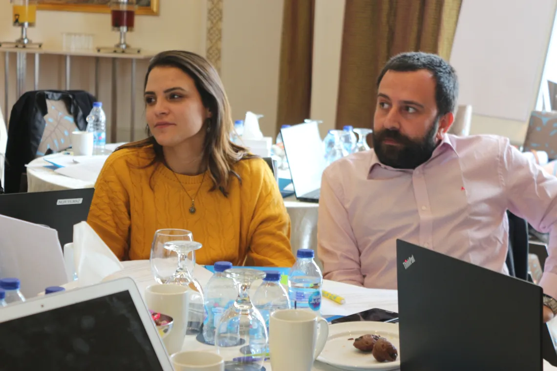 A woman and a man sitting at a table and listening to other participants