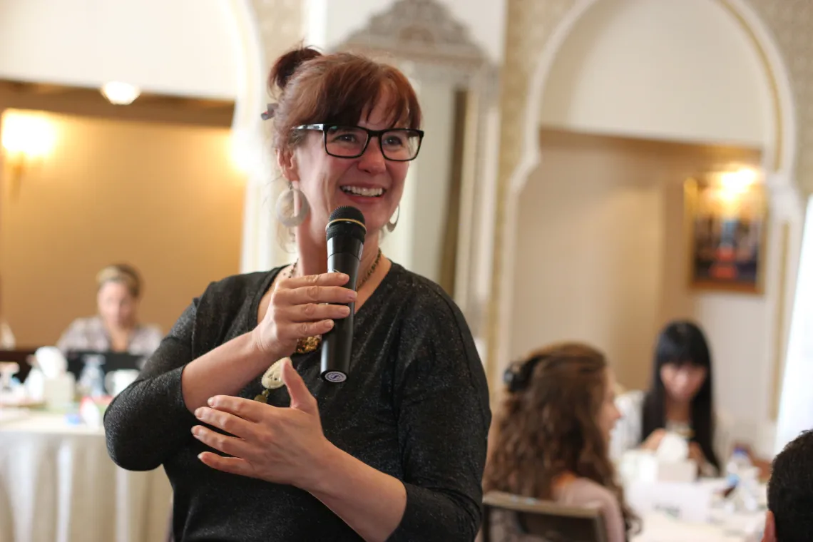 A woman is standing up, speaking in a micro and smiling