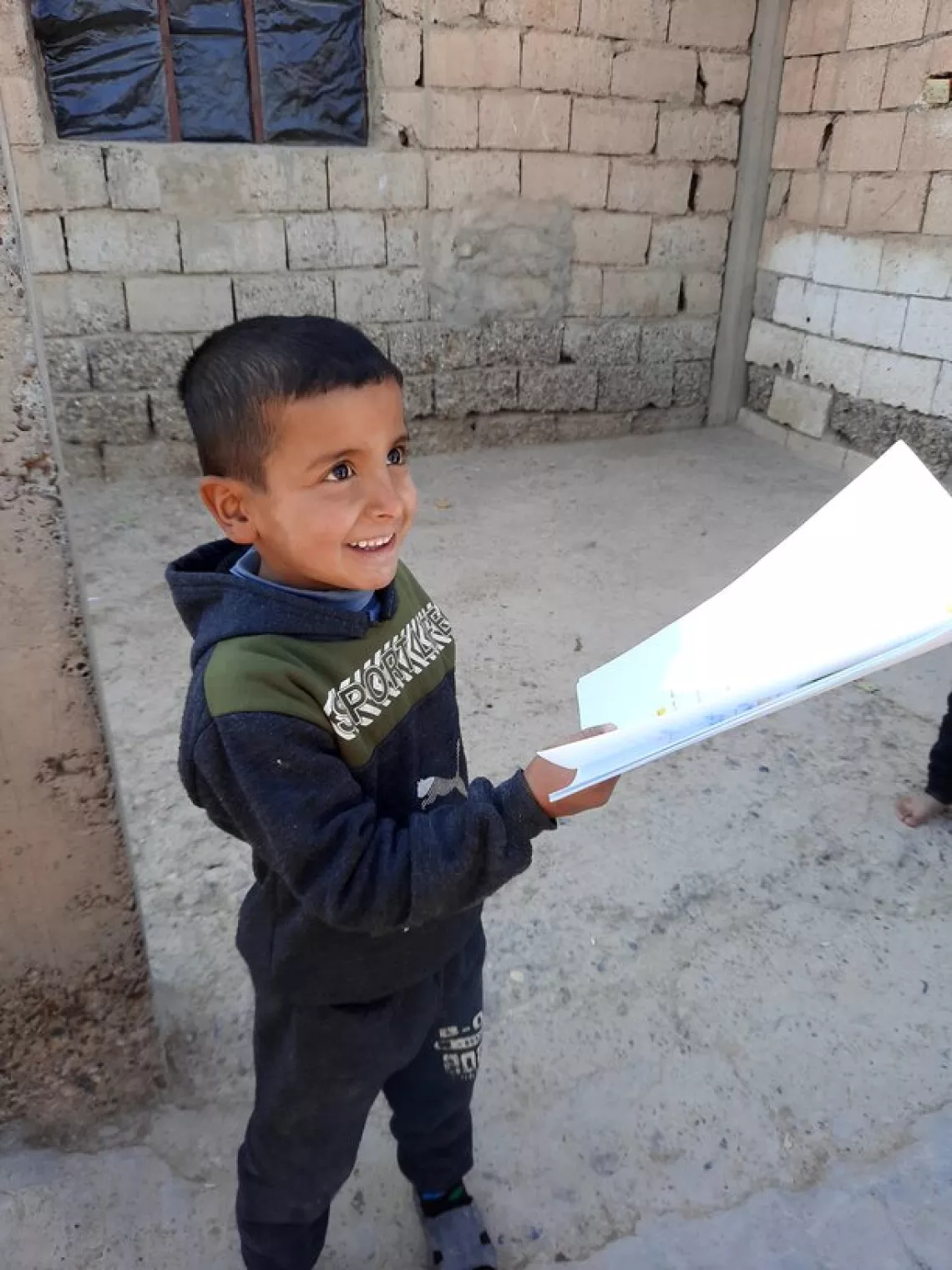A young boy is smiling and handling papers, outside