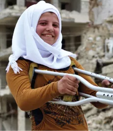 A young girl with crutches is smiling, standing outside