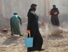 Three women cleaning a construction site, digging in the sand.